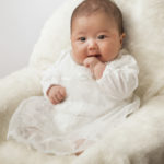 可愛らしい仕草の椅子に座ったドレスの赤ちゃん