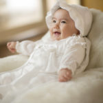 椅子に座って笑うベビードレスを着た100日赤ちゃん