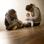 床に座った百日の赤ちゃんと両親